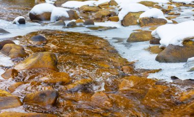 Küçük donmuş dere taşların üzerinden akıyor, kış dağı nehir manzarası.