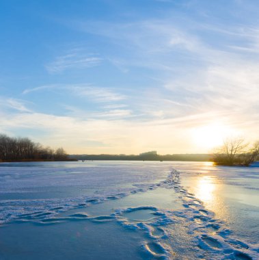 Kış donmuş nehir, gün batımında kıyıda ormanla kaplı karla kaplıydı.