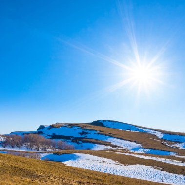 Parlak güneşli bir günde karla kaplı çimlerle kaplı dağ vadisi