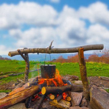 Yeşil dağların arasında kamp ateşinde ısınan turistik kazan, açık hava seyahat kampı sahnesi