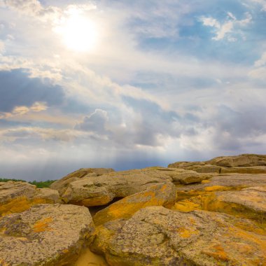 Tepenin yamacında parıldayan güneşin altında kocaman taşlar var.