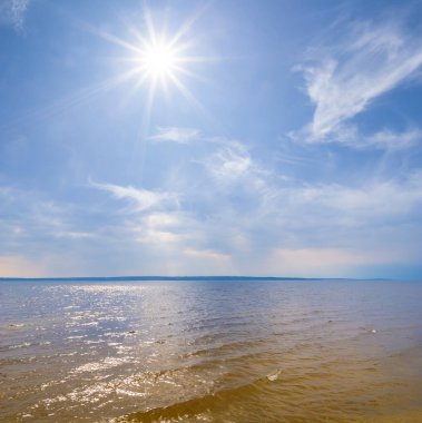 Işıl ışıl güneş ve yoğun bulutların altında geniş sakin bir deniz koy.