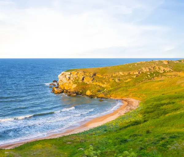 Sahilde yeşil tepeleri olan sakin bir deniz koyunda, günbatımında sakin bir deniz koyunda kayalık bir pelerin.