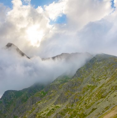 Yoğun siste yeşil dağ zincirleri ve parlak güneşin altında bulutlar.