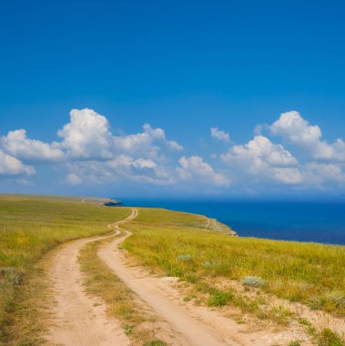 Denizin yukarısındaki çayırların arasında bükülmüş toprak yol