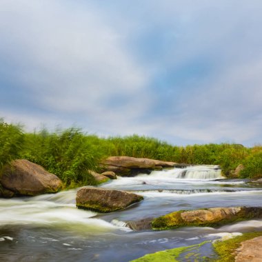 Nehir, parlak bir yaz gününde büyük bir taşın üzerinden akıyor.