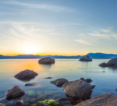 Sakin deniz koyunda, sahilde taşlarla birlikte dramatik günbatımında.