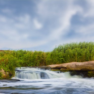 Nehir, parlak bir yaz gününde büyük bir taşın üzerinden akıyor.