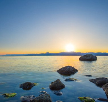 Sakin deniz koyunda, sahilde taşlarla birlikte dramatik günbatımında.