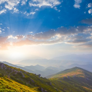 Gün batımında bulutlar içinde yeşil dağ vadisi, yaz dağ yolculuğu sahnesi