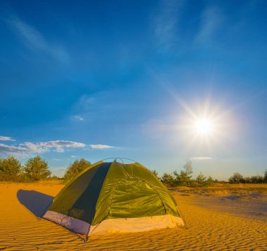 Küçük yeşil turistik çadır güneşli bir günde kumlu çölde kalır.