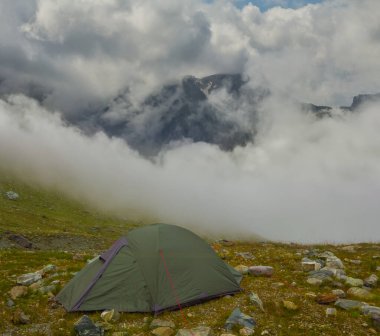Küçük turistik çadır yoğun sis ve bulutların içinde dağda kalır.