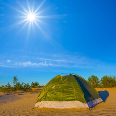 Küçük yeşil turistik çadır güneşli bir günde kumlu çölde kalır.