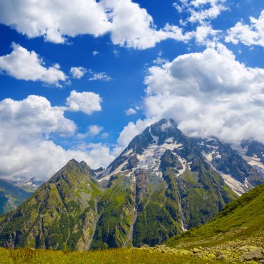 Yoğun bulutlu gökyüzünün altında, karda yeşil dağ sırtı