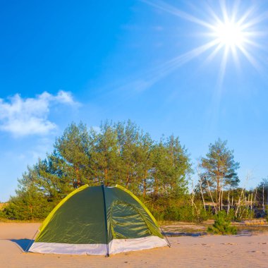 Küçük yeşil turistik çadır güneşli bir günde kumlu çölde kalır.