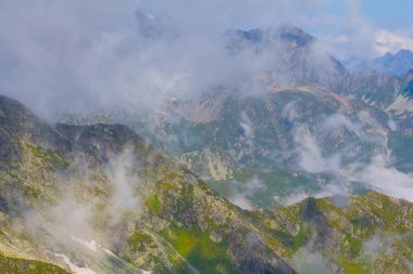 Yoğun sisli yeşil dağ vadisi ve mavi bulutlu gökyüzünün altındaki bulutlar