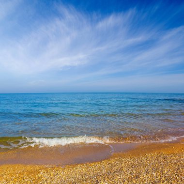 Mavi bulutlu gökyüzünün altında kumlu kumlu bir sahil.