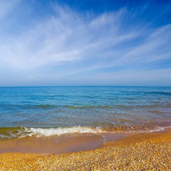 Mavi bulutlu gökyüzünün altında kumlu kumlu bir sahil.