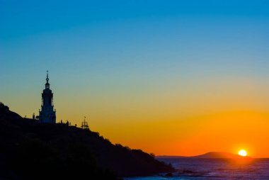 Gün doğumunda deniz pelerininde Hristiyan kilisesi silueti