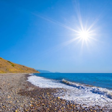 Yazın güneşli bir günde kıyıya yakın büyük taşlarla taşlı bir sahil.