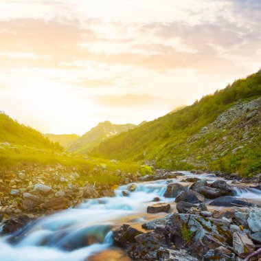 Dağ nehri gün batımında taşların üzerinden akıyor. Akşam dağları manzarası.