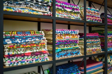 Bir tekstil mağazasındaki ahşap raflarda bulunan renkli Özbek ikat kumaşları, canlı desenler ve Özbekistan 'ın zengin kültürel mirası sergiliyor.