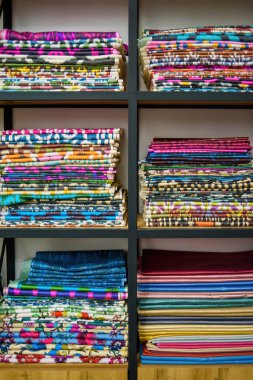 Bir tekstil mağazasındaki ahşap raflarda bulunan renkli Özbek ikat kumaşları, canlı desenler ve Özbekistan 'ın zengin kültürel mirası sergiliyor.