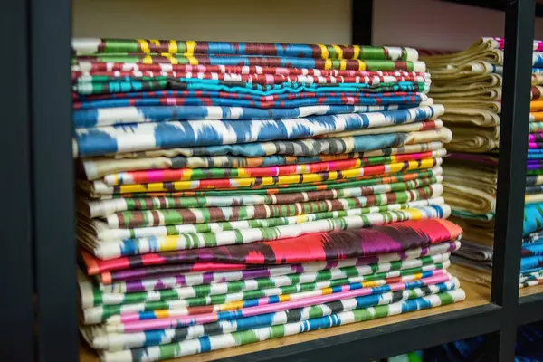 Bir tekstil mağazasındaki ahşap raflarda bulunan renkli Özbek ikat kumaşları, canlı desenler ve Özbekistan 'ın zengin kültürel mirası sergiliyor.