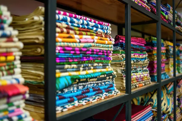 Bir tekstil mağazasındaki ahşap raflarda bulunan renkli Özbek ikat kumaşları, canlı desenler ve Özbekistan 'ın zengin kültürel mirası sergiliyor.