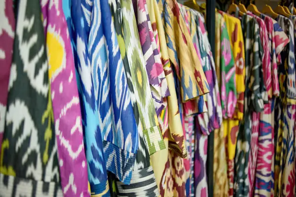 Özbekistan 'ın zengin kültürel mirası ve canlı desenler sergileyen renkli geleneksel Özbek kaftanları bir tekstil mağazasında asılı duruyor.