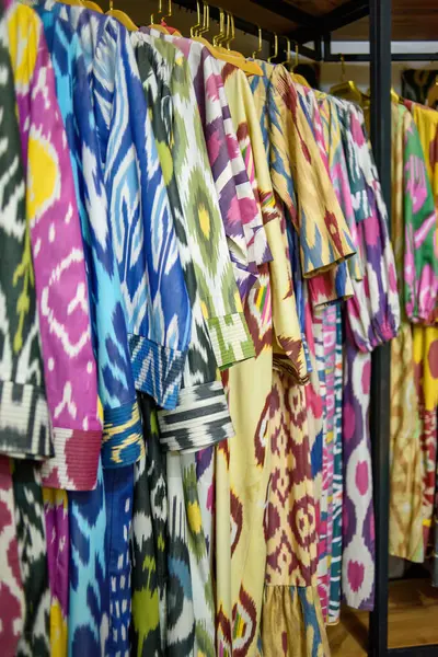 Özbekistan 'ın zengin kültürel mirası ve canlı desenler sergileyen renkli geleneksel Özbek kaftanları bir tekstil mağazasında asılı duruyor.