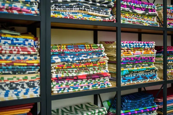 Bir tekstil mağazasındaki ahşap raflarda bulunan renkli Özbek ikat kumaşları, canlı desenler ve Özbekistan 'ın zengin kültürel mirası sergiliyor.