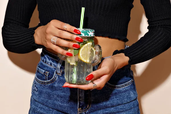 Bir mojito bardağı tutan eller, kokteyl ve kırmızı manikürlü bir kızın güneşli bir yaz fotoğrafı.