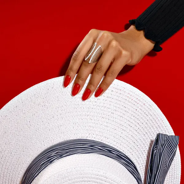 hand with a red manicure holding a hat