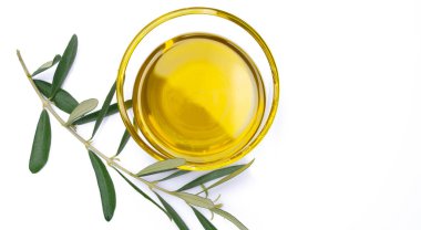 Yanında zeytin yaprakları olan cam kasede organik zeytin yağı.