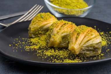 Siyah arka planda fıstıklı midye şeklinde baklava.