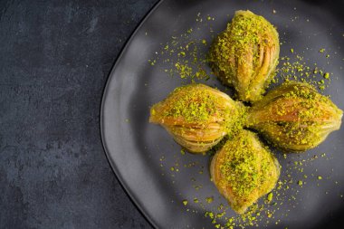 Siyah arka planda fıstıklı midye şeklinde baklava.