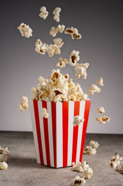 Gri arka planda izole edilmiş kırmızı ve beyaz çizgili kağıt kutuda patlamış mısır.