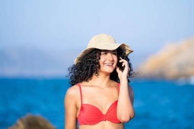 Güzel genç kız sahilde cep telefonuyla konuşuyor.