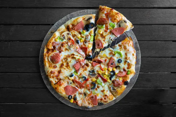 Tahta arka planda dilimlenmiş karışık pizza.