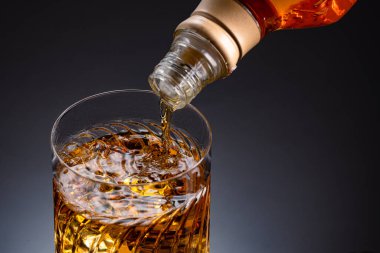 Siyah arka planda buz küpleri olan bir bardak viski. Viski şişeden bardağa dökülürken