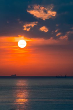 Gün batımında ve gün doğumunda ufukta kargo gemilerinin siluetleri beliriyor.