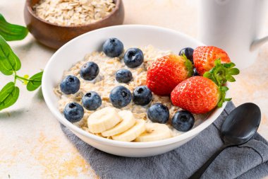 Kahvaltı için yaban mersinli, çilekli ve muzlu sütlü lapa.