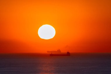 Gün batımında ve gün doğumunda ufukta kargo gemilerinin siluetleri beliriyor.