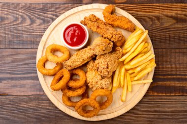 Tavuk filetosu, kanat, soğan halkası ve ahşap arka planda patates kızartması.