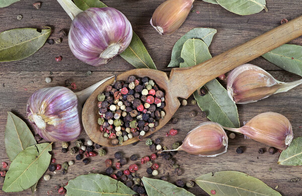 traditional spices for the kitchen. bay leaf, mixture of various peppers in a spoon and garlic on a wooden table. top view