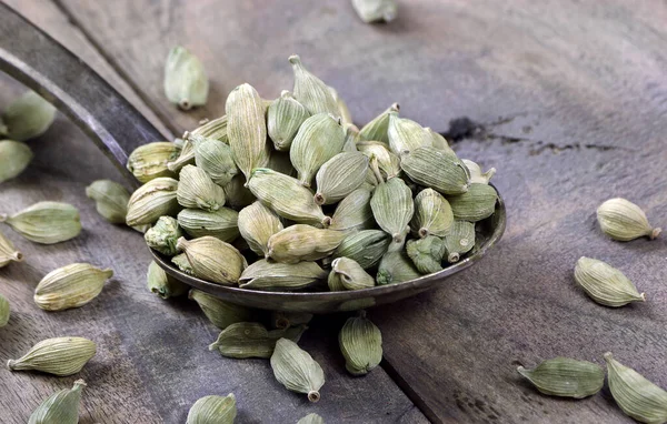 stock image green cardamom pods in a spoon on a wooden table