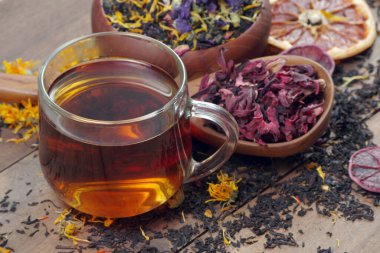 Bir fincan taze çay ve ahşap bir masada farklı çay yaprakları. Çiçek yapraklarıyla karıştırılmış çay, ahşap kaşıkta amber çiçeği ve kurutulmuş sitruslar. Kapat.