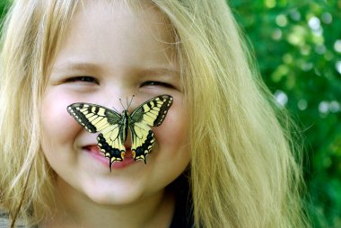Kelebek bir çocuğun üzerinde oturuyor. Kelebekli çocuk. Kelebek machaon küçük bir kız üzerinde. Seçici odak. Kırlangıç kuyruğu kelebeği, Papilio maçaonu.