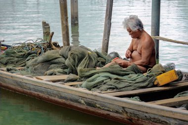 Chantaburi, Tayland, 21 Mart 2023: Bir balıkçı ahşap teknesinde oturmuş balık ağını onarıyor.